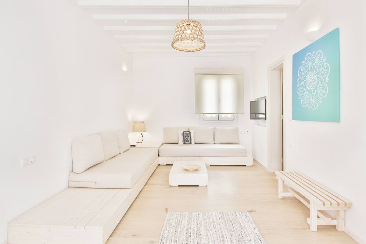A modern living room with a sofa, a coffee table, a bench, a hanging light fixture, and a wall-mounted TV.