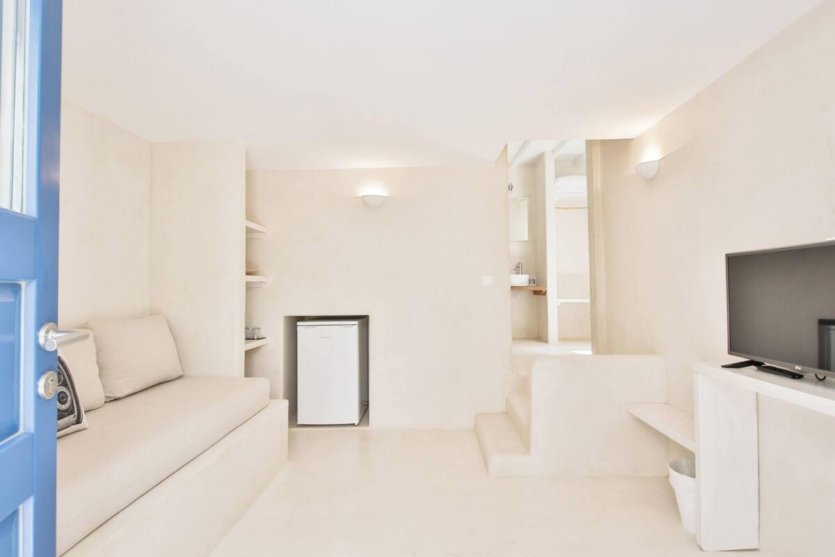 A modern, minimalist room with a sofa, a small refrigerator, a TV, and built-in shelving.