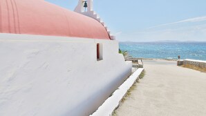 A white building with a pink dome and a bell tower, overlooking a coastal view. - Baba Houlakia (Mykonos)