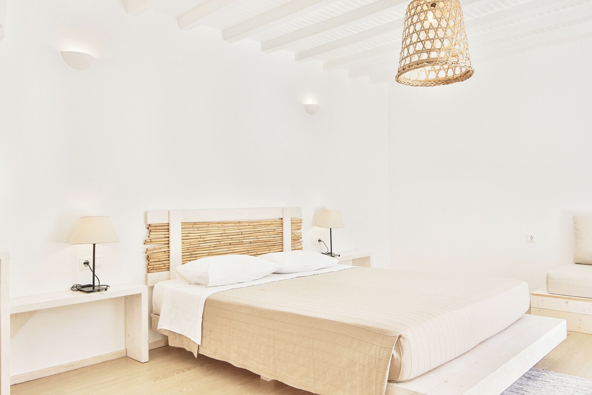 A minimalist bedroom with a large bed, bedside tables, and a hanging light fixture.