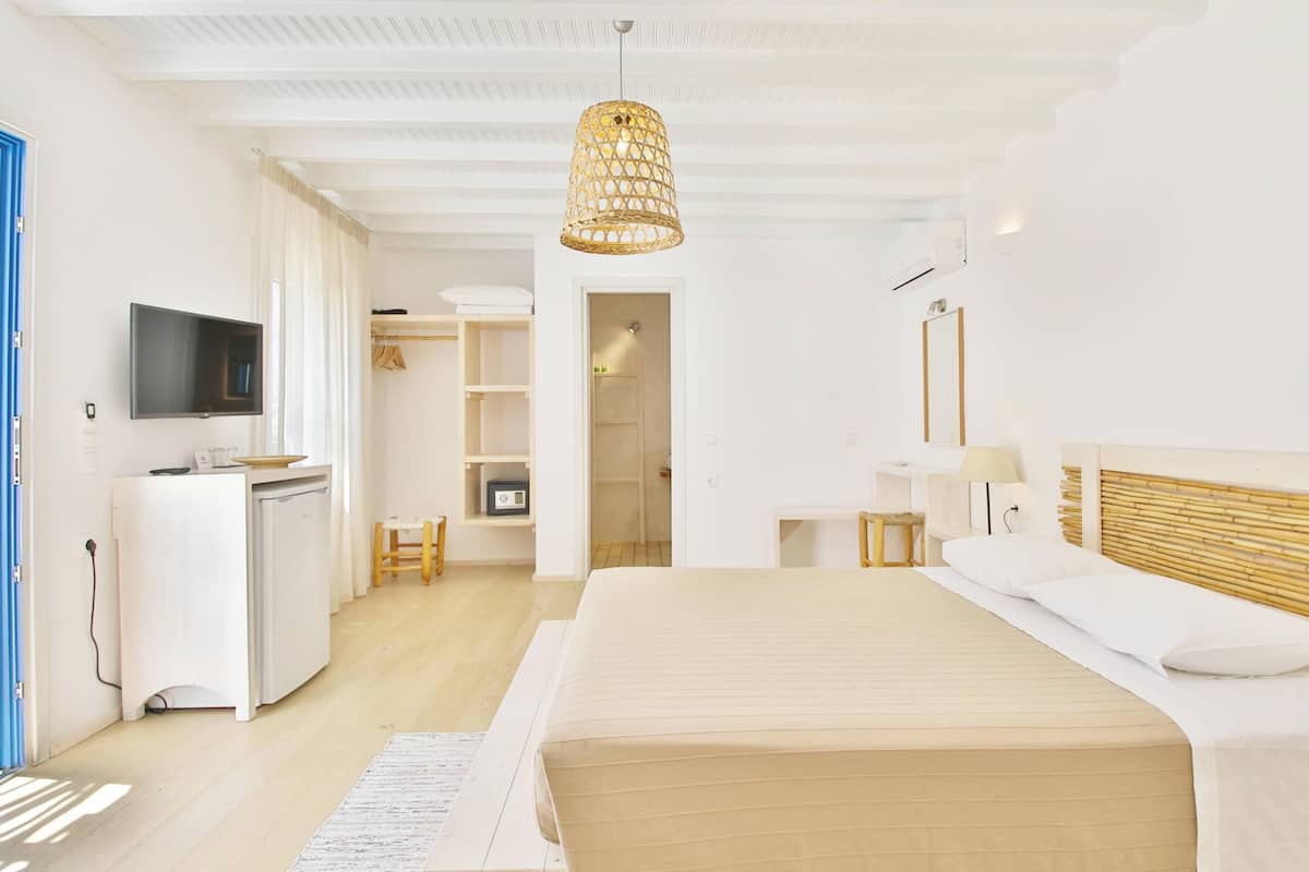 A modern hotel room with a bed, bedside table, lamp, TV, wardrobe, and a kitchenette.