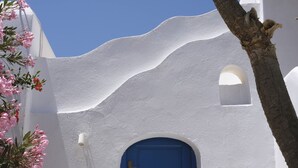 A white building with a blue door and a small arched window. - Baba Houlakia (Mykonos)