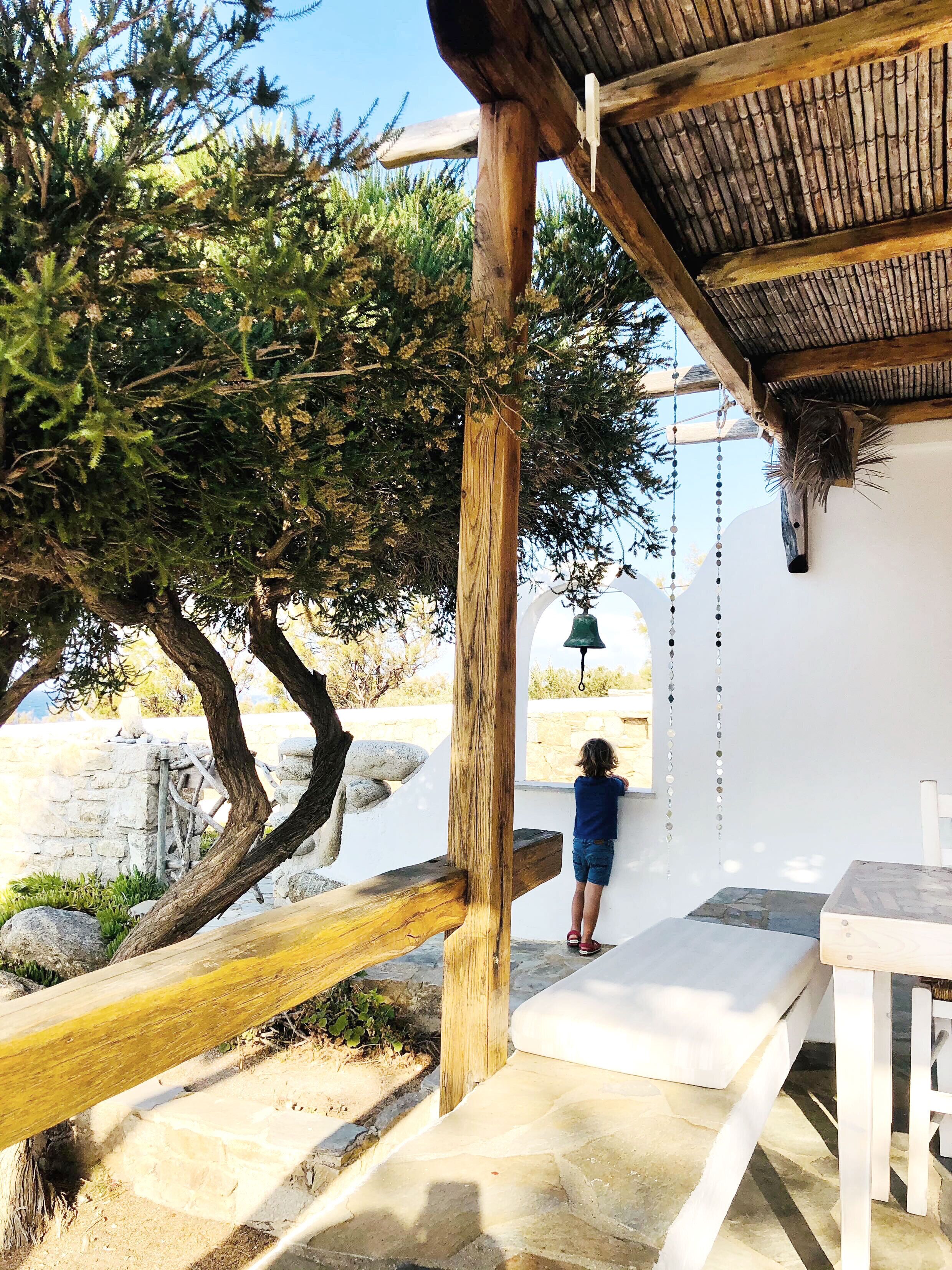 A wooden structure with a thatched roof, a stone wall, and a child standing by a white wall.