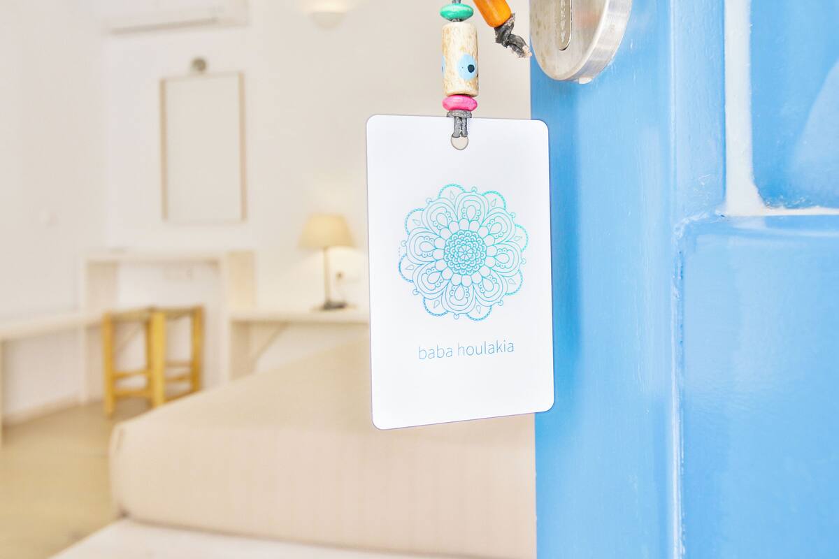 A card with a mandala design and the text "baba houlikia" hanging on a blue wall.