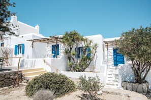 Un edificio blanco con puertas y ventanas azules, una escalera de piedra y un pequeño jardín con plantas.