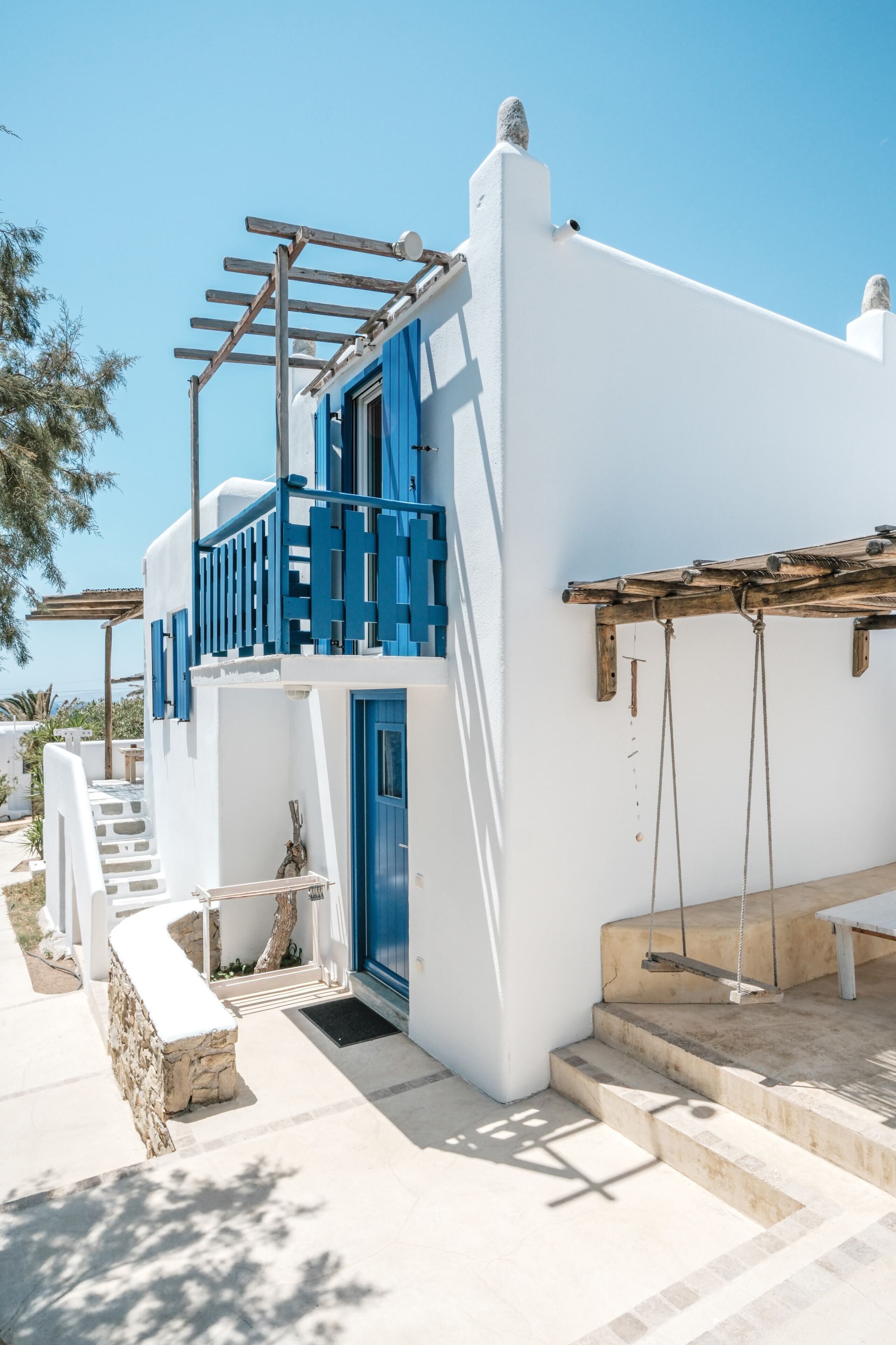 Un bâtiment blanc agrémenté de touches de bleu, une pergola en bois et un banc en pierre.