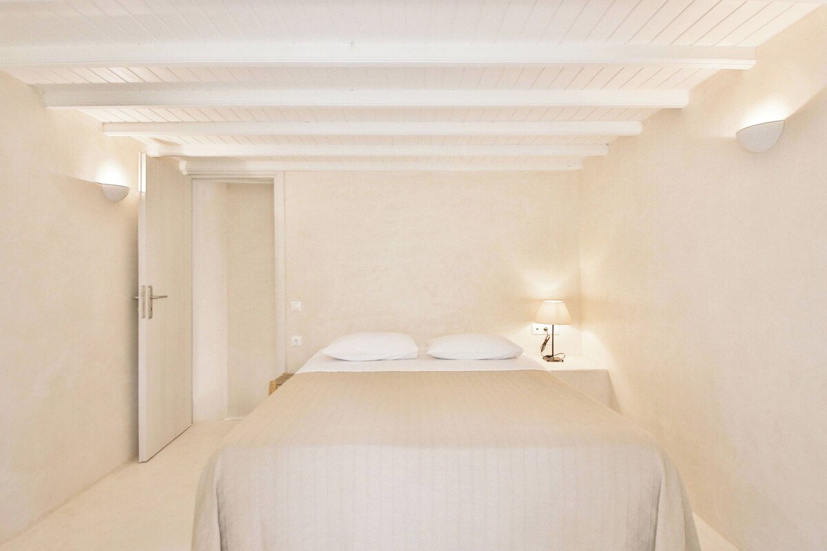 A bedroom with a bed, a nightstand, a lamp, and a door.