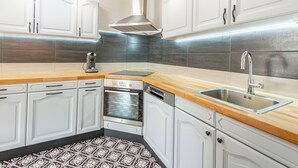 Una cocina moderna con armarios blancos, un lavamanos de acero inoxidable, un horno empotrado y una cafetera.