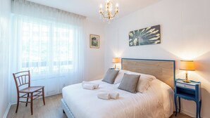 Habitación de hotel con una cama grande, cabecera de madera, candelabro, una silla y una mesita de noche con lámpara.