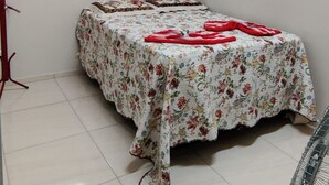 A room with a wooden ceiling, a bed with a floral bedspread, a window with blinds, and a standing fan.