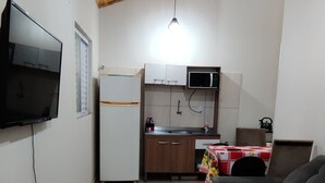 A compact living space with a wooden ceiling, a flat-screen TV mounted on the wall, a kitchenette with a microwave, and a sofa.