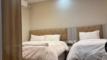 Habitación de hotel con dos camas, suelo de madera, diseño moderno en el techo y una mesita de noche con lámpara.