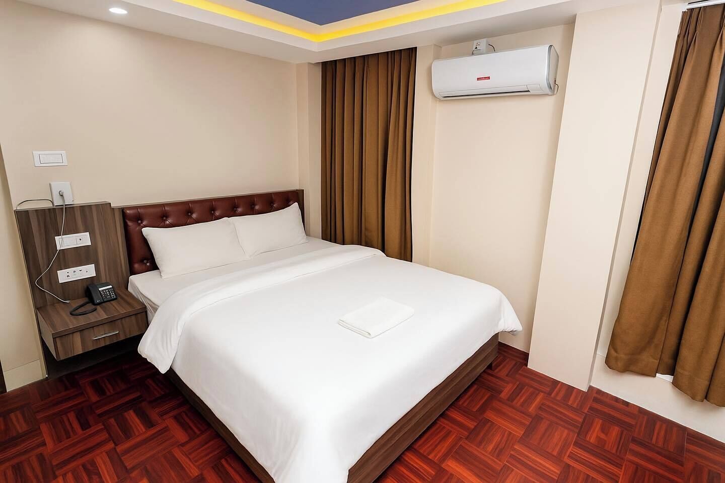 Quarto de hotel com cama, mesa de cabeceira com telefone, ar condicionado e piso de madeira.