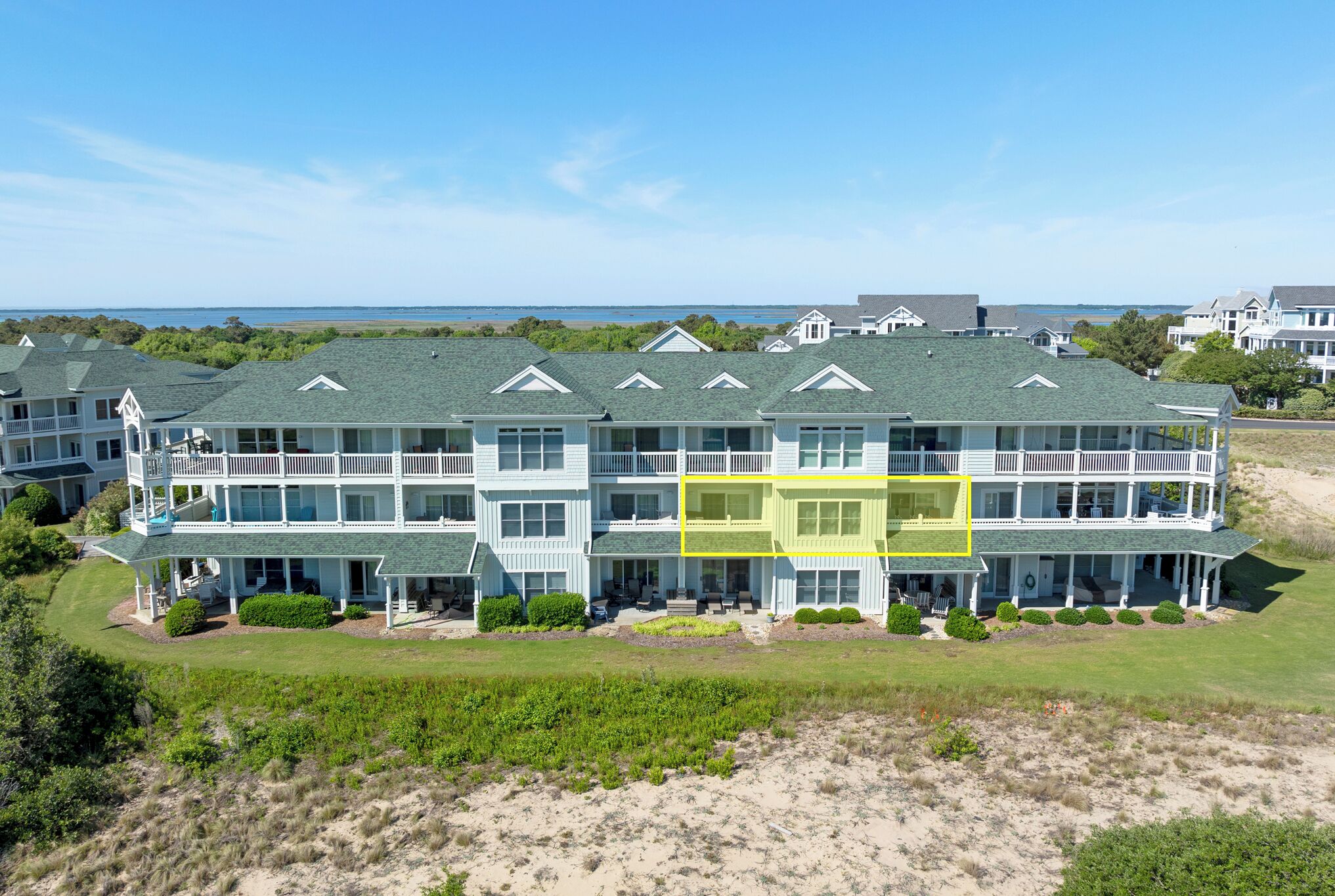 A multi-story beachfront hotel with balconies, a covered patio, and a view of the ocean.