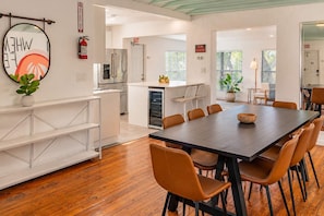 A modern kitchen with white cabinetry, a dining area with a dark wooden table and brown chairs, and a view of the adjacent living space.