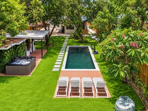 A backyard with a swimming pool, a hot tub, and a deck area with lounge chairs.