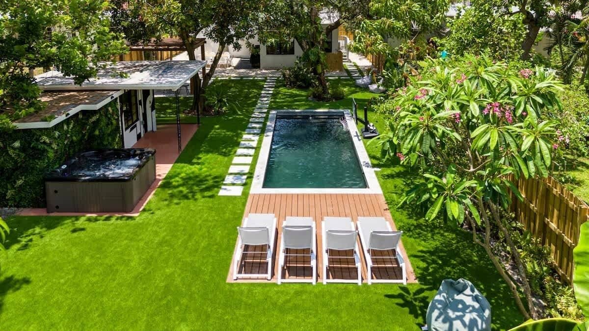 A rectangular swimming pool with a wooden deck and white lounge chairs.