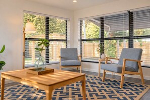 Une pièce avec deux chaises grises, une table en bois et un sol recouvert d’un tapis à motifs géométriques.