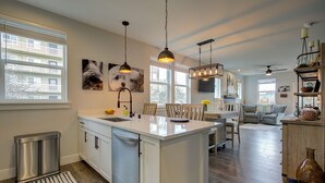 Una cocina moderna con una isla central, iluminación colgante y vistas al salón.