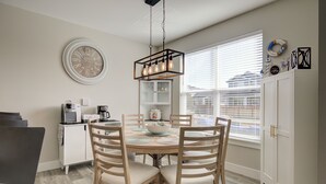 Un comedor con una mesa redonda, sillas de madera, una lámpara colgante, un reloj y una ventana con persianas.