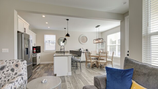 Una cocina moderna con una isla central, un comedor con mesa y sillas de madera, y una sala de estar con sofá y mesa de centro.