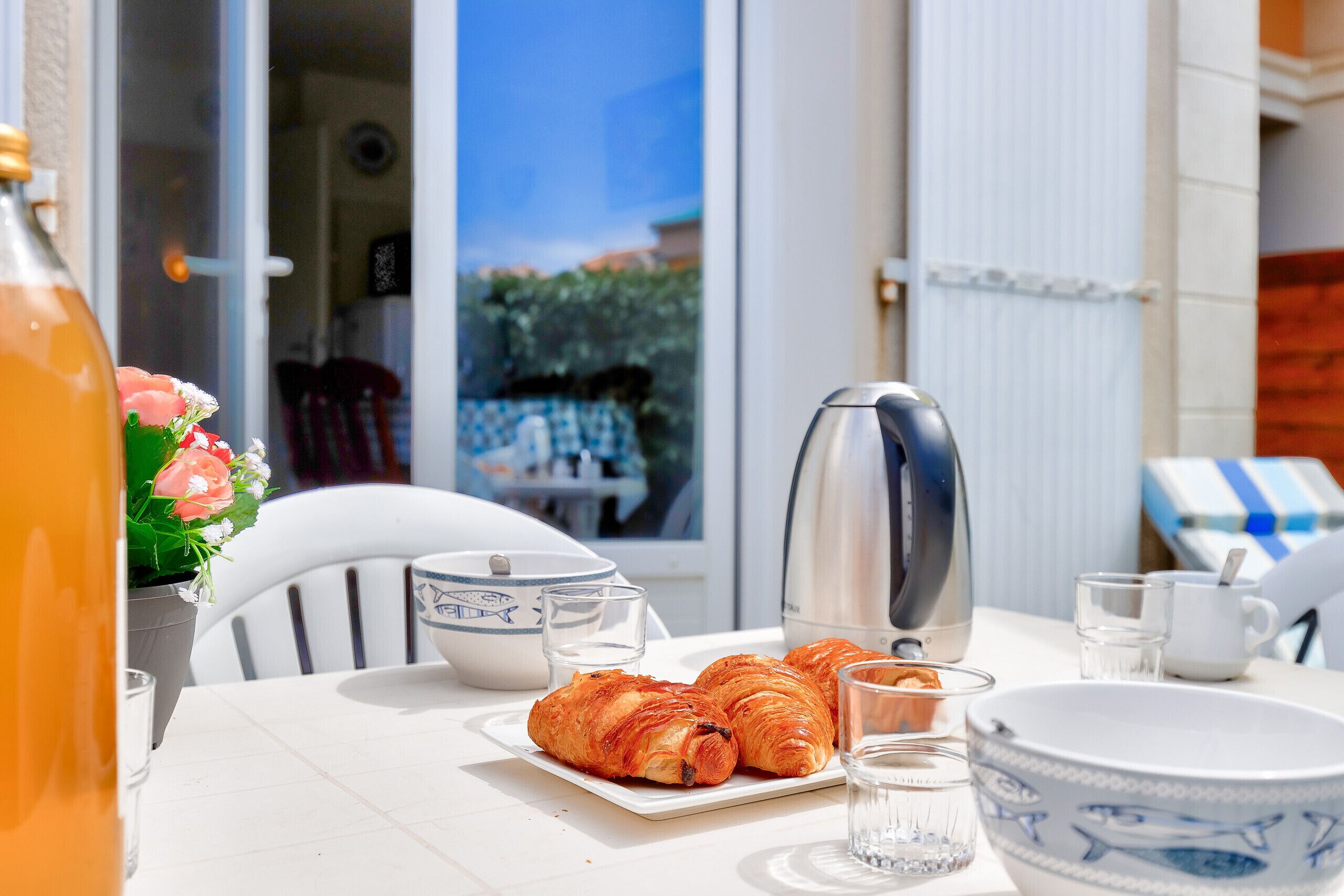A table set with croissants, a coffee maker, and a bottle of orange juice.