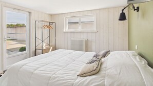 Un dormitorio con cama, ventana, radiador y lámpara colgante.