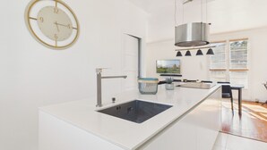 Una cocina moderna con una isla central, un reloj en la pared y un amplio ventanal con persianas.