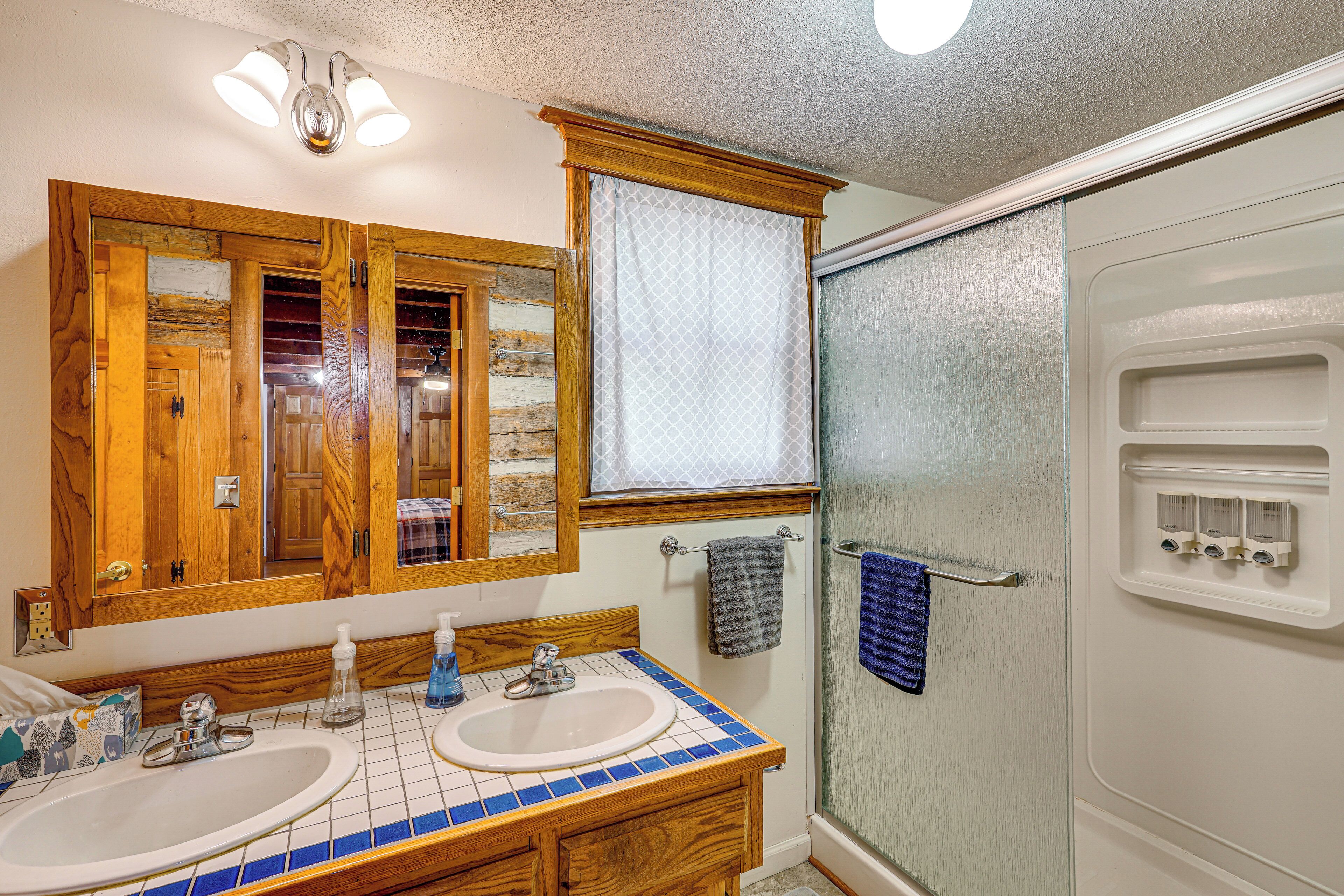 A bathroom with two sinks, wooden cabinets, a mirror, and a shower.
