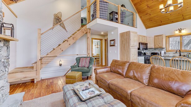 A spacious living area with a wooden staircase, a leather sofa, and a dining area with wooden chairs. - Jeffersonville Home w/ Deck Near Hiking & Climbing (Jeffersonville)