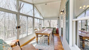 A sunroom with large windows, a wooden dining table, and a cozy seating area. - Jeffersonville Home w/ Deck Near Hiking & Climbing (Jeffersonville)