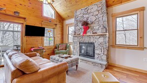 A cozy cabin interior with a stone fireplace, leather furniture, and large windows. - Jeffersonville Home w/ Deck Near Hiking & Climbing (Jeffersonville)
