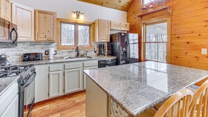 A kitchen with wooden cabinets, granite countertops, a stove, refrigerator, and a large window. - Jeffersonville Home w/ Deck Near Hiking & Climbing (Jeffersonville)