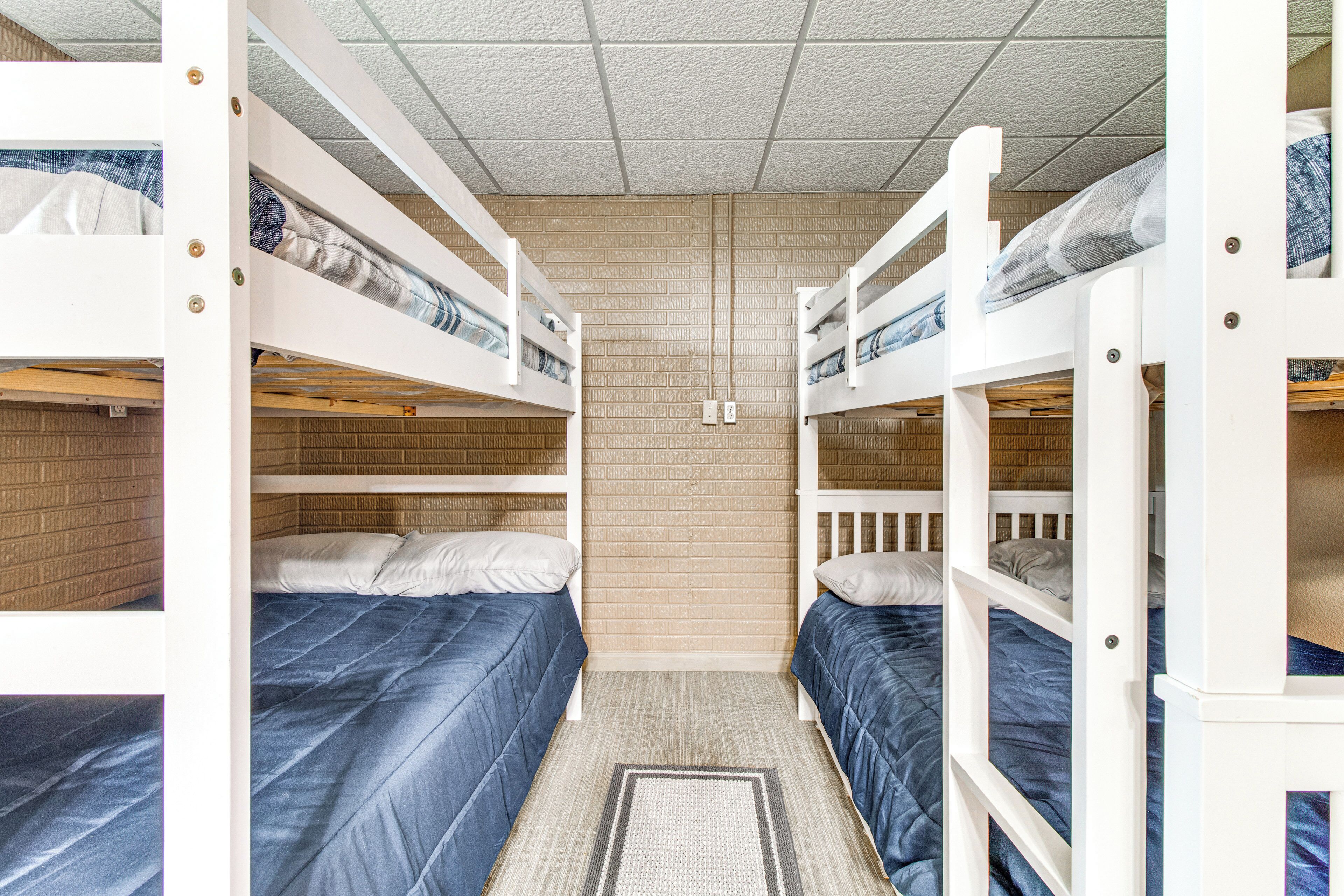 A dormitory room with bunk beds, a brick-patterned wall, and a ceiling with a grid design.