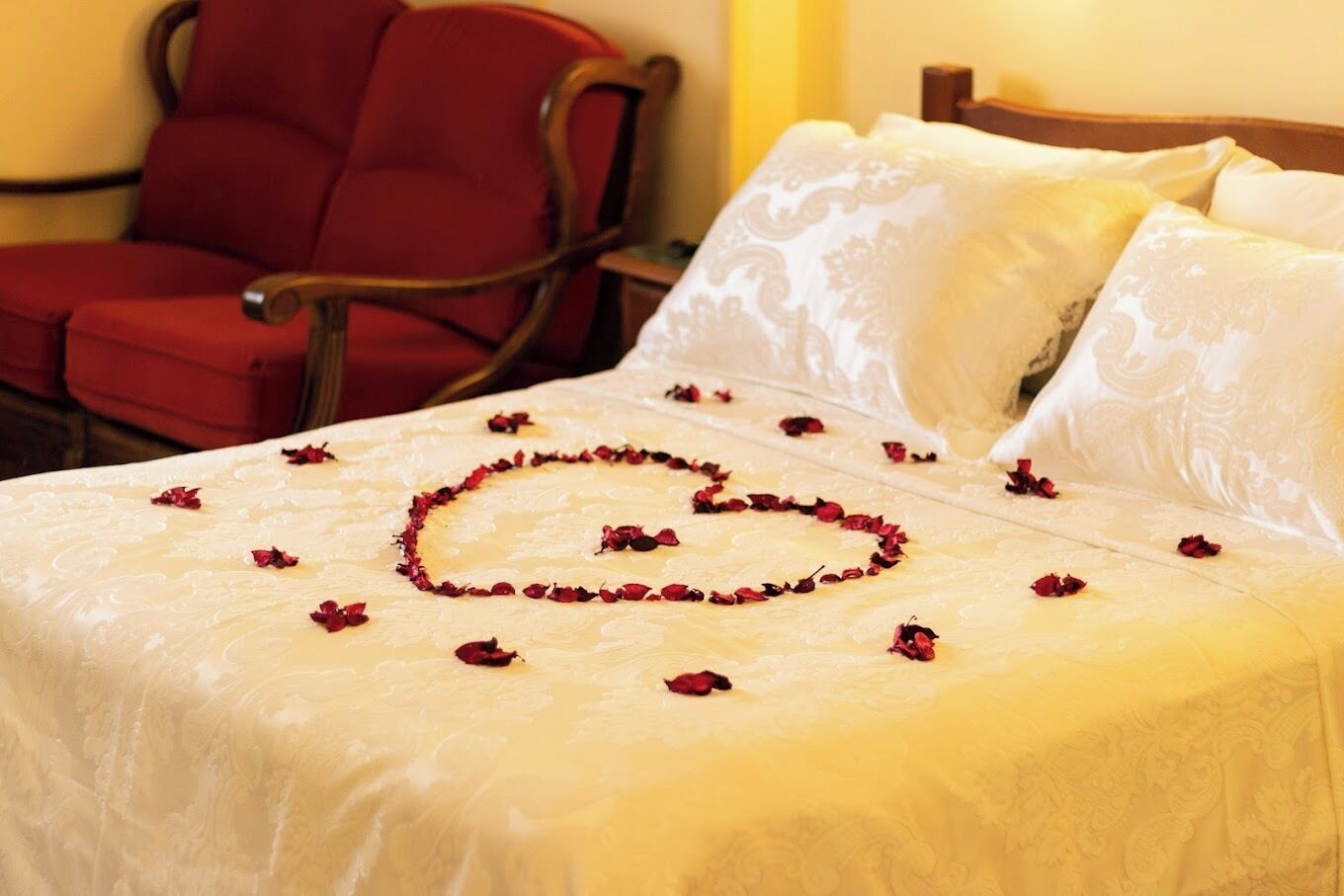 A bed with a heart-shaped arrangement of rose petals on the bedspread.