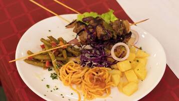 Een bord eten met spaghetti, groene bonen, een koolsalade, ananasstukjes en spiezen met vlees.