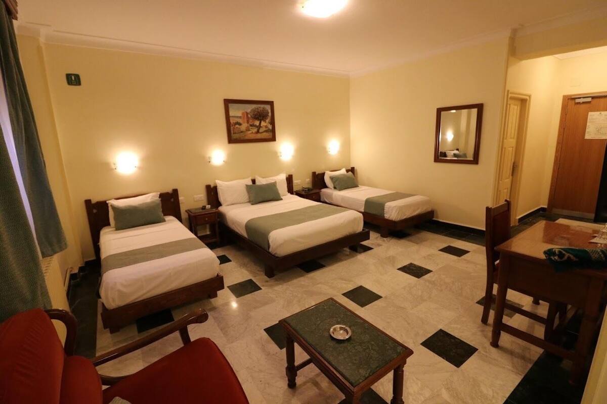 Habitación de hotel con tres camas, una mesita, una silla y un escritorio.