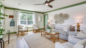 Una sala de estar con ventilador de techo, un sofá, sillas, una mesa de centro y una ventana con cortinas.