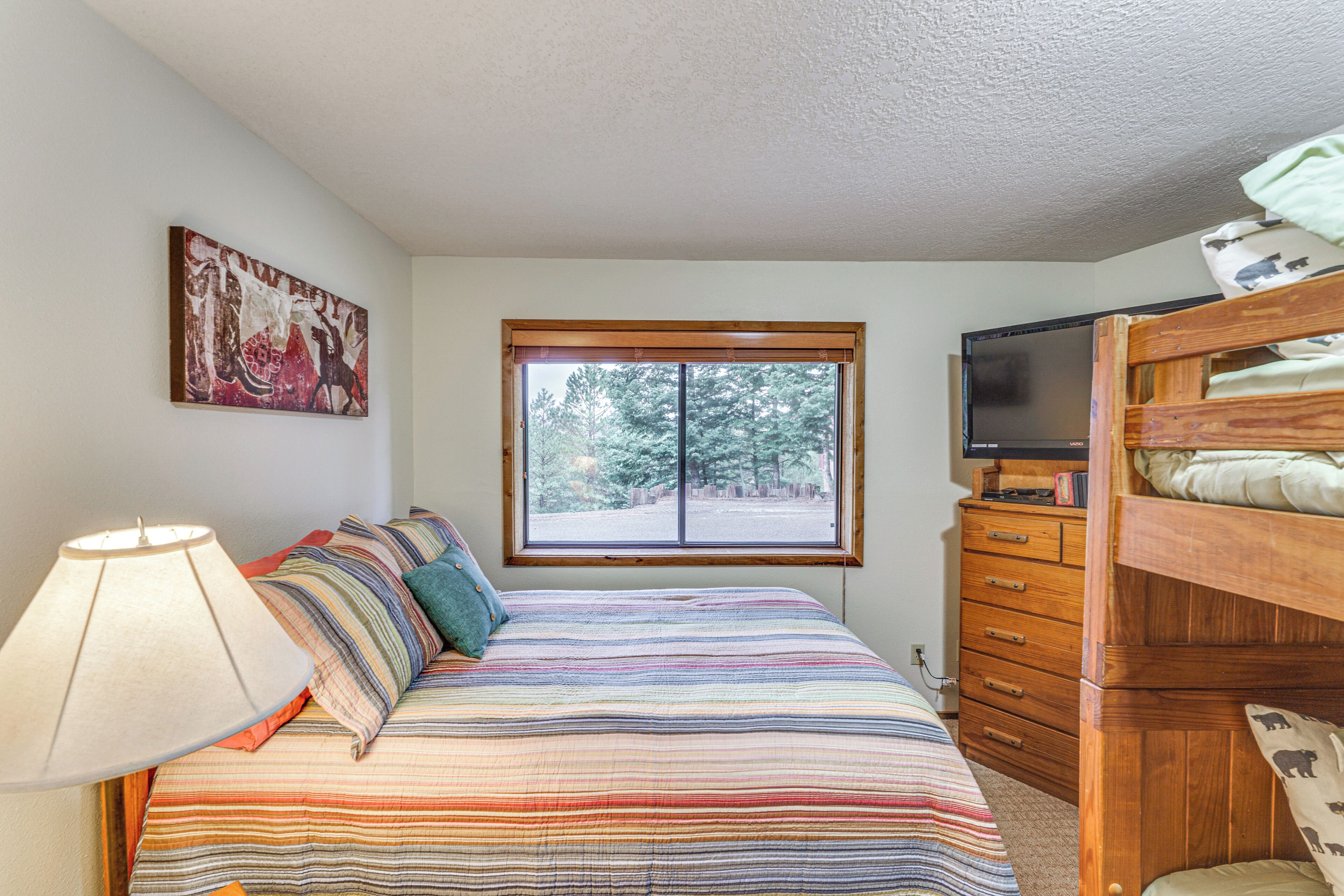 A bedroom with a bed, a window, a dresser, and a television.