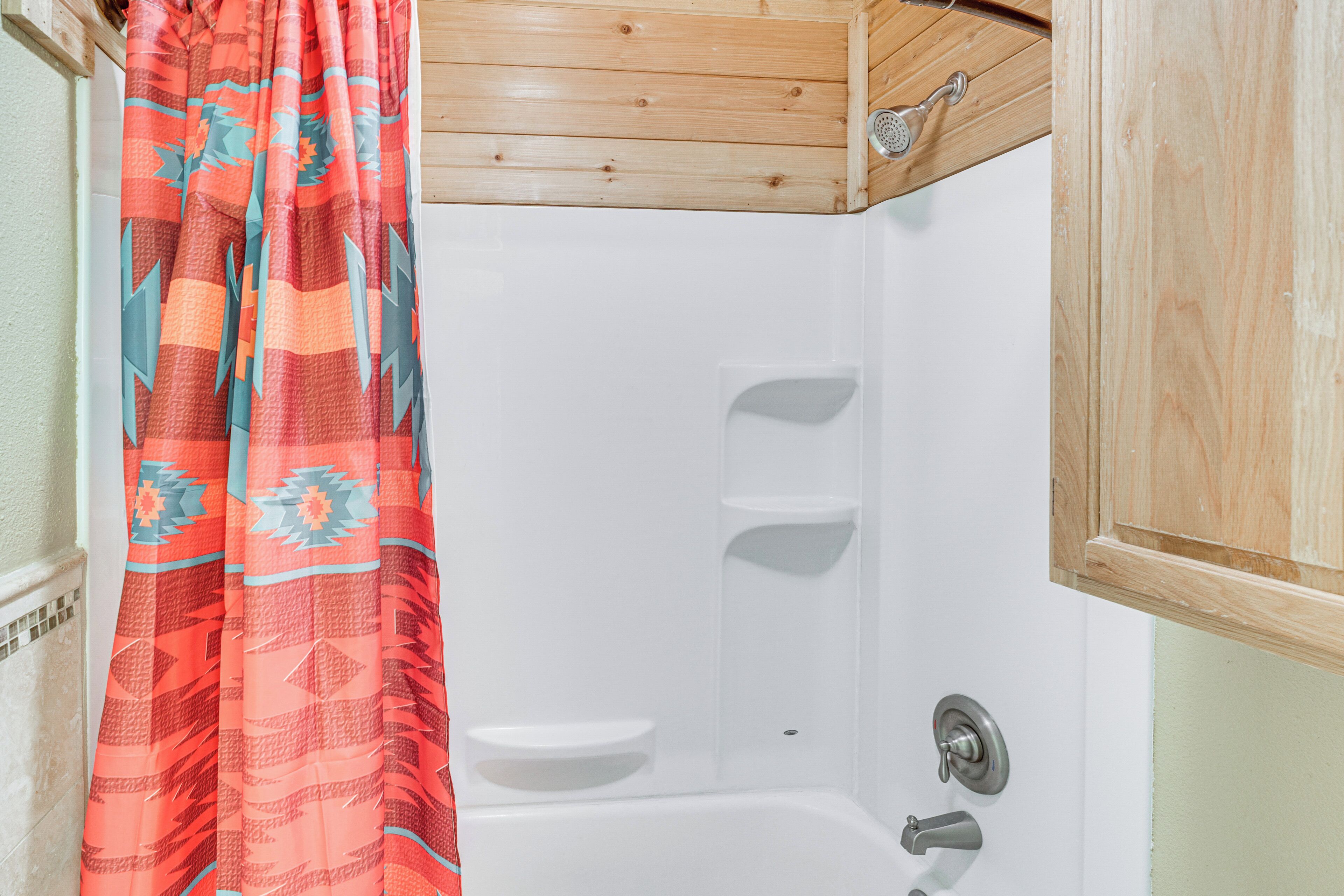 A bathroom with a shower, a wooden cabinet, and a patterned shower curtain.