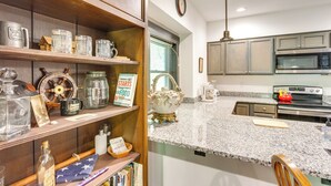 A kitchen with granite countertops, stainless steel appliances, wooden shelves, and a clock on the wall. - Jasper Apartment w/ Patio & Creek Access (Jasper)
