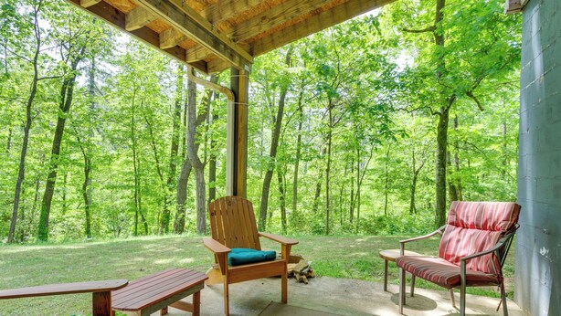 A covered outdoor seating area with two wooden chairs and a bench, surrounded by a forest. - Jasper Apartment w/ Patio & Creek Access (Jasper)