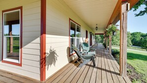 A covered porch with wooden flooring, green chairs, and a view of a grassy area. - Neosho Home on 90 Acres w/ Private Pool & Fire Pit (Neosho)