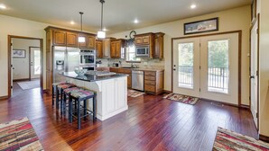 A spacious kitchen with wooden cabinets, stainless steel appliances, and a central island with bar stools. - Neosho Home on 90 Acres w/ Private Pool & Fire Pit (Neosho)