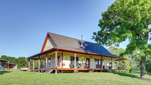 A two-story house with a porch, a chimney, and a large tree in front. - Neosho Home on 90 Acres w/ Private Pool & Fire Pit (Neosho)