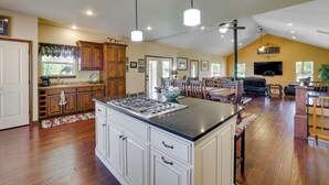 A spacious kitchen with a large island, wooden cabinets, and a dining area with a TV and seating. - Neosho Home on 90 Acres w/ Private Pool & Fire Pit (Neosho)
