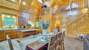 L’intérieur d’une cabane en bois comprend un coin repas, une cuisine et un escalier menant à un niveau supérieur.