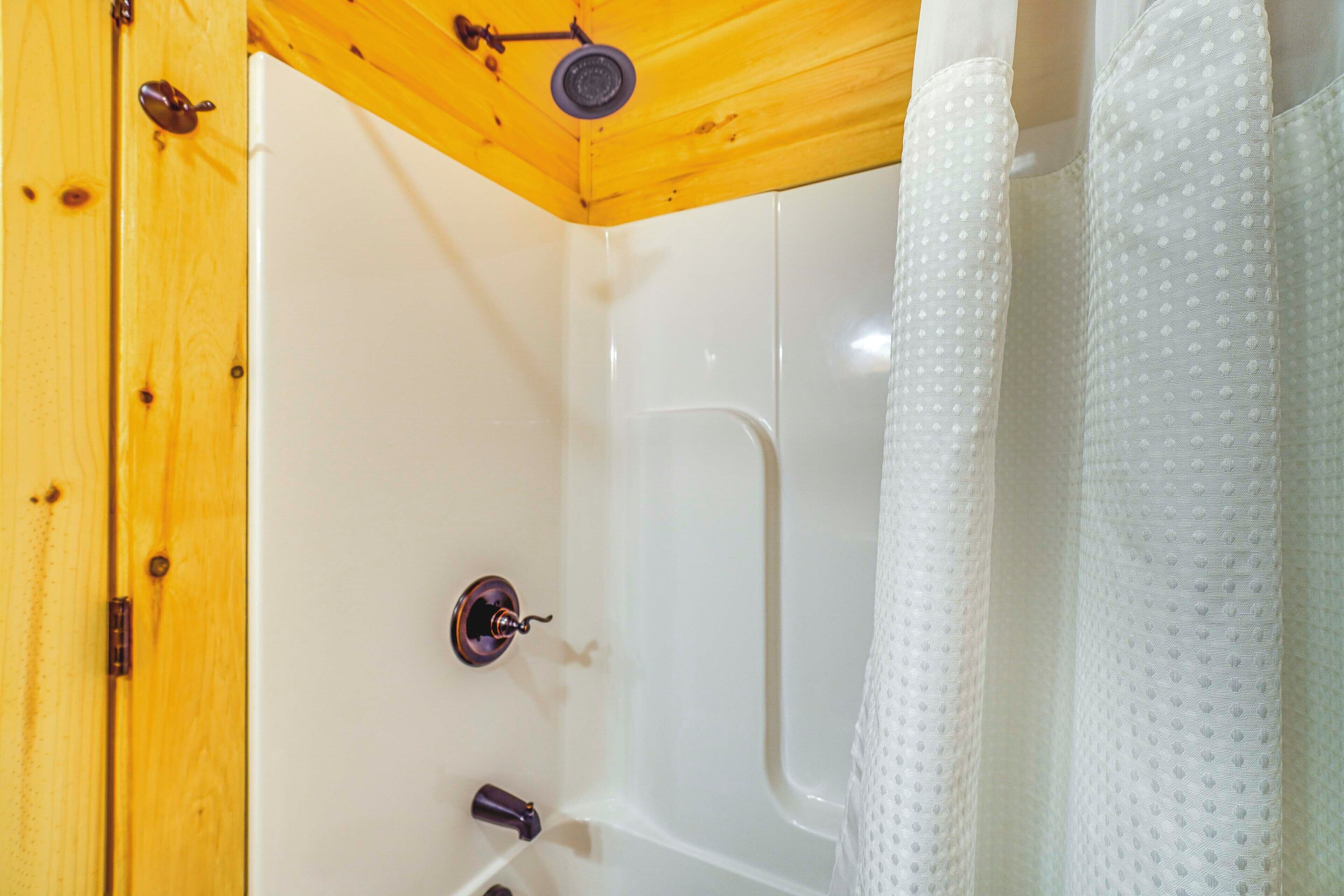 Een badkamer met een houten plafond, een wit bad en een douchegordijn.