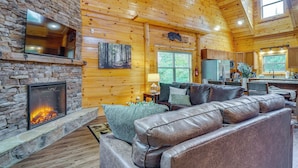 L’intérieur d’une cabane en rondins, avec une cheminée en pierre, un canapé en cuir et un coin cuisine.