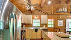 A kitchen with wooden cabinets, a stainless steel refrigerator, granite countertops, and a ceiling fan. - Updated Mtn Cabin on 20 Acres w/ Large Waterfall (Jasper)